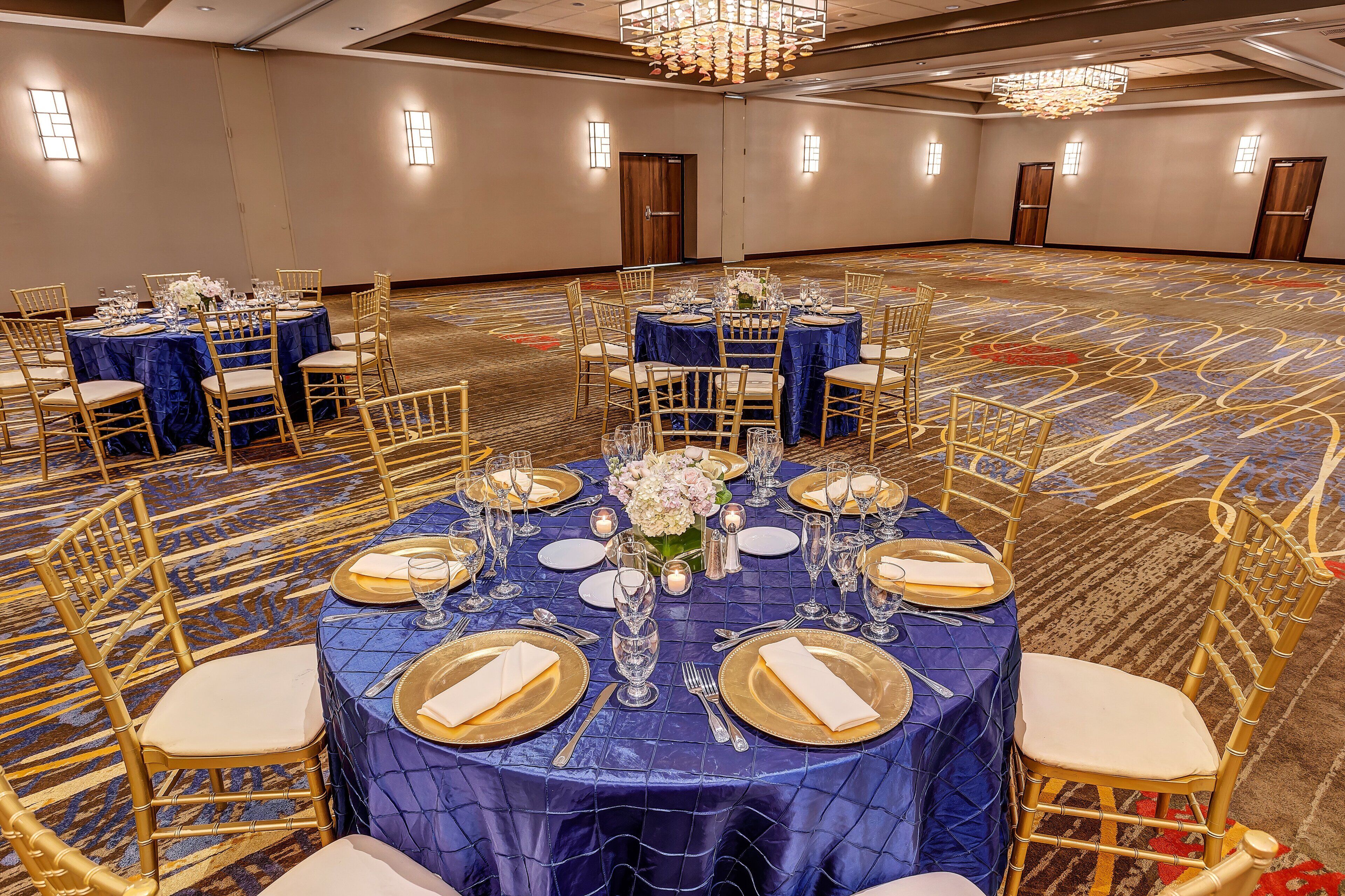 Un salón de banquetes con mesas redondas dispuestas para cenar, con manteles azules y sillas doradas.