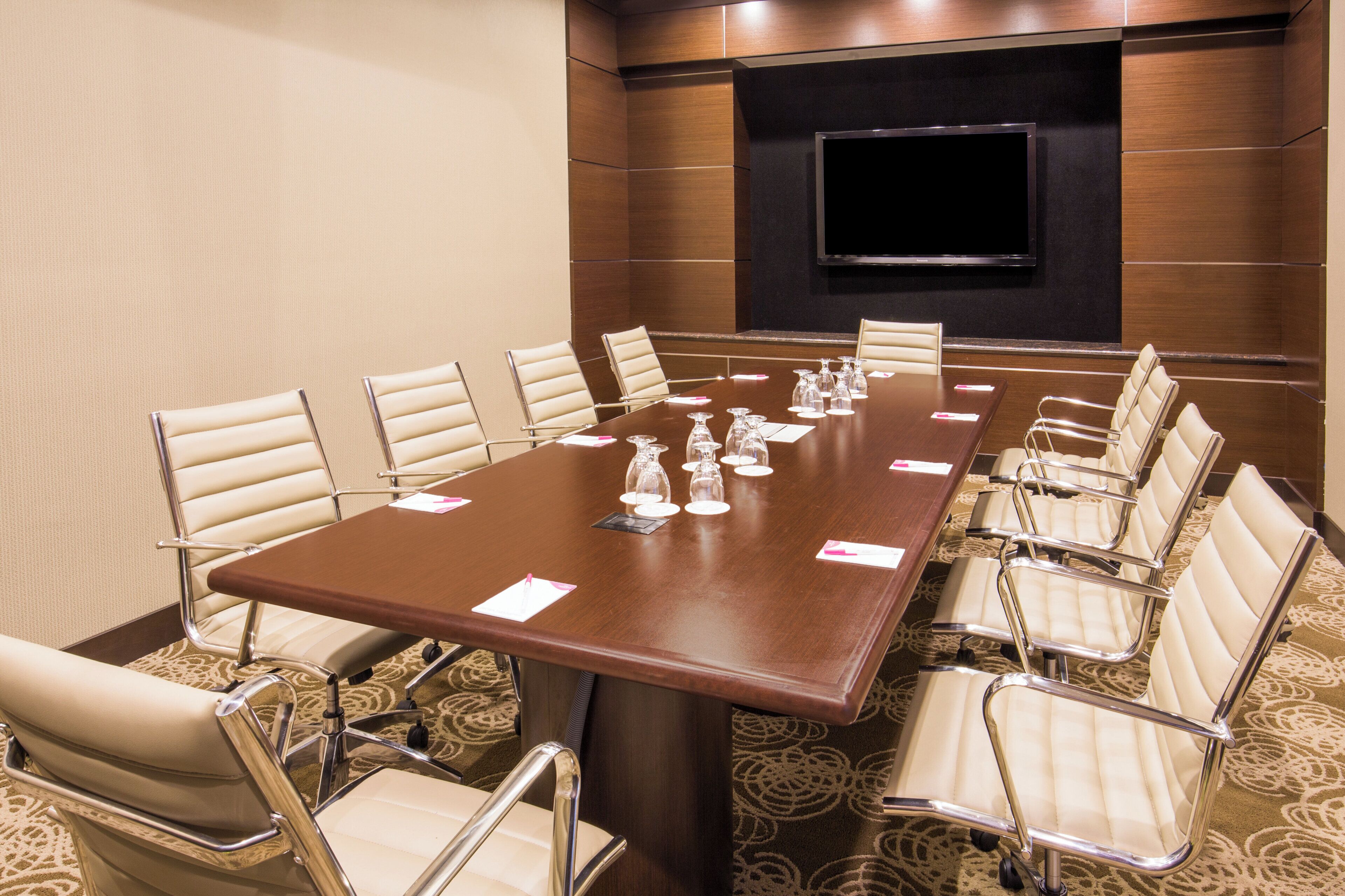 A conference room with a large table, chairs, a flat-screen TV, and a carpeted floor.
