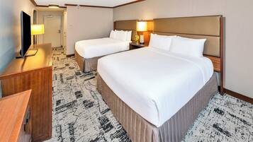 A hotel room with two beds, a desk, a TV, and a lamp.