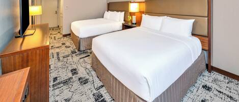 A hotel room with two beds, a desk, a TV, and a lamp.