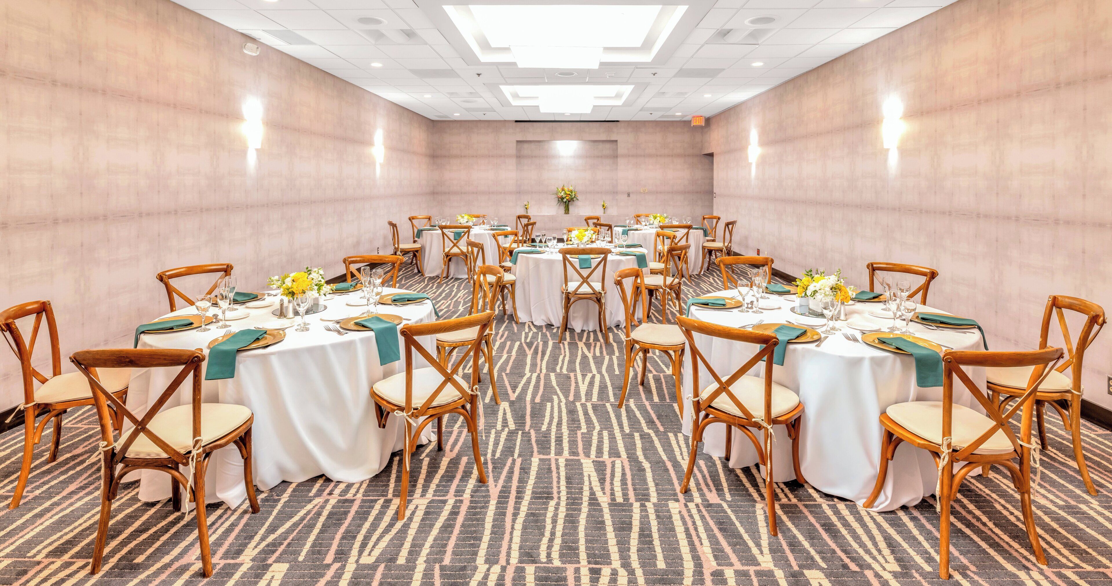 A conference room with round tables, wooden chairs, and white tablecloths.