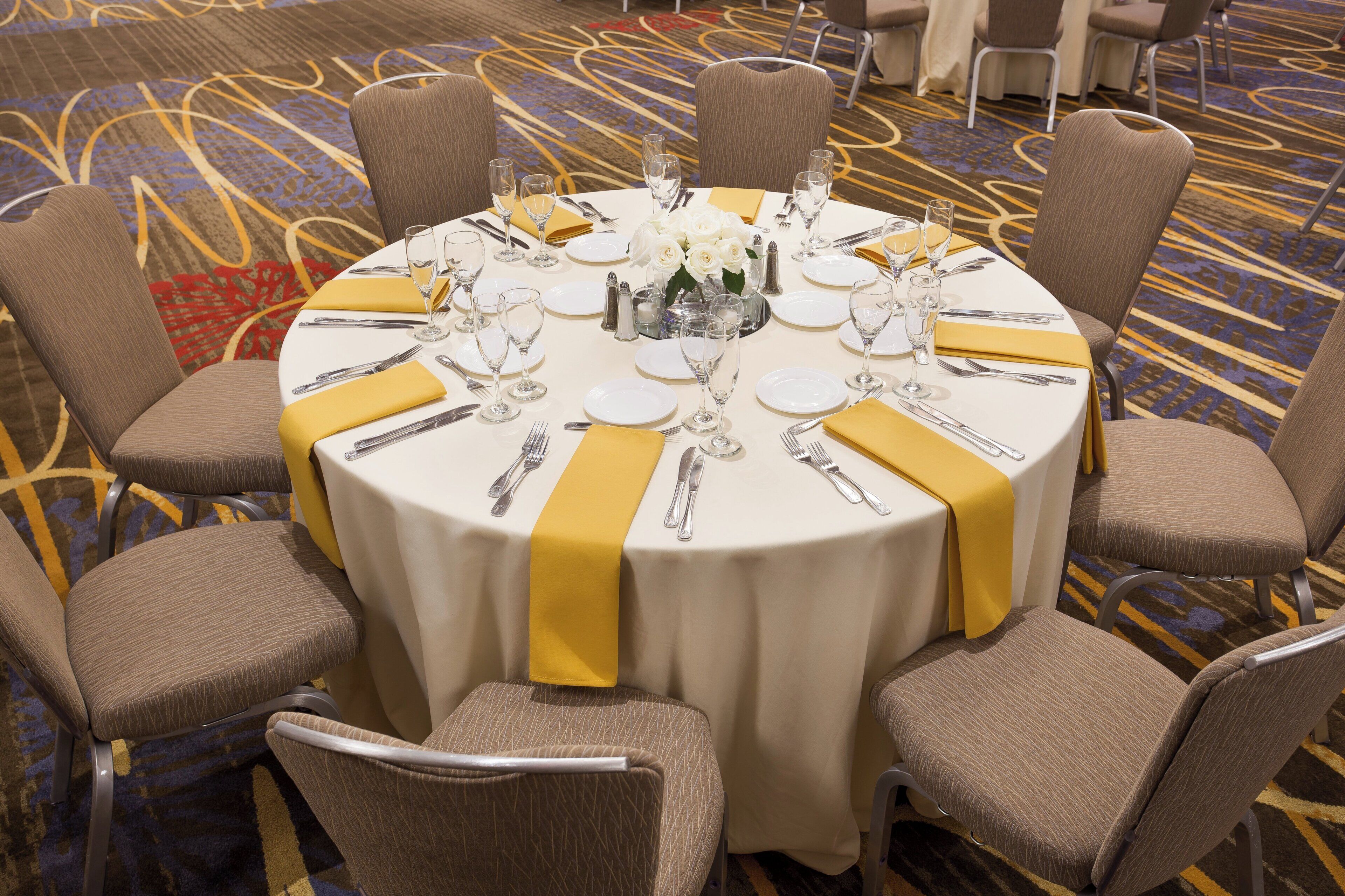 A round dining table with a yellow table runner, surrounded by six upholstered chairs.