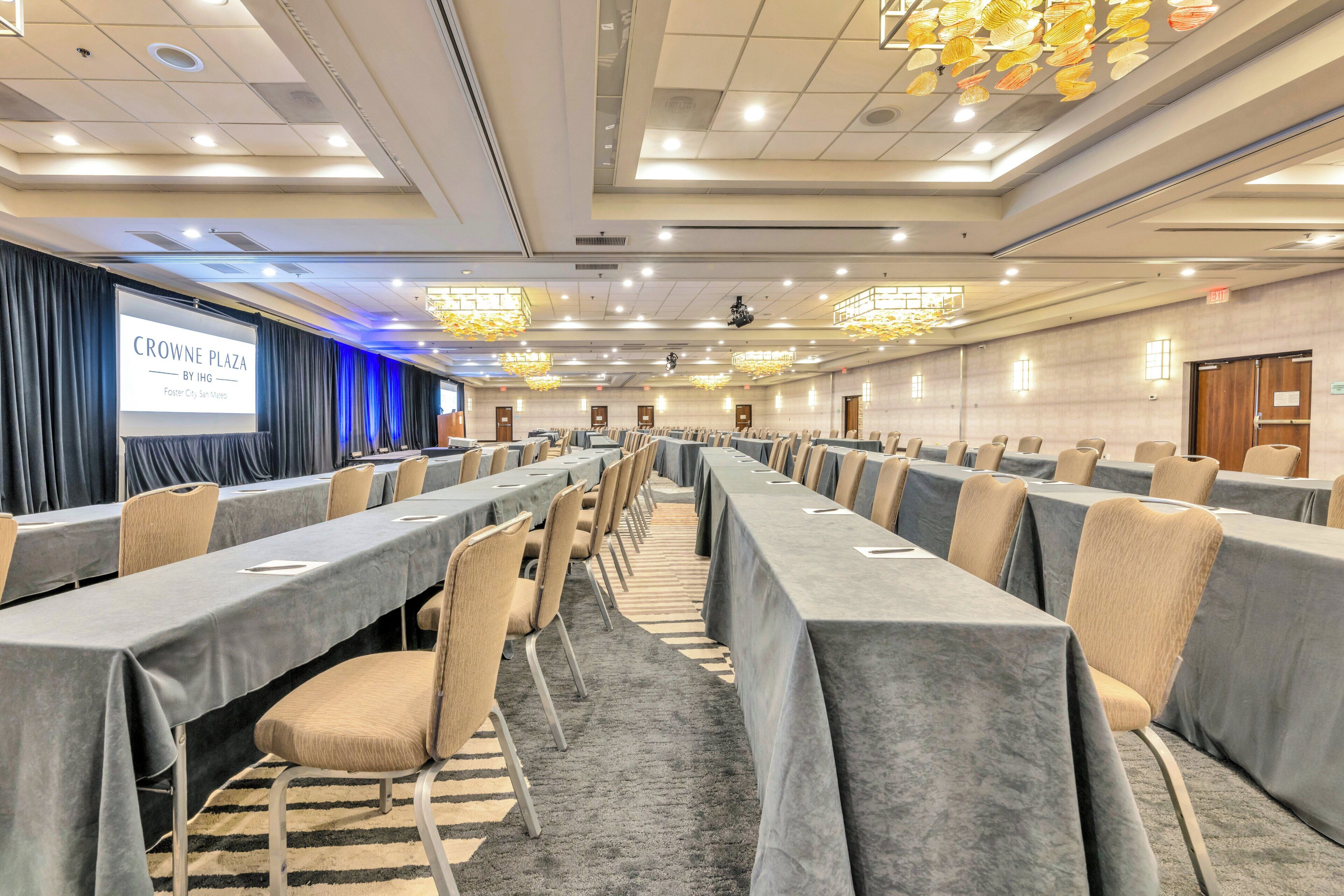 A conference room with long tables, chairs, and a presentation screen.
