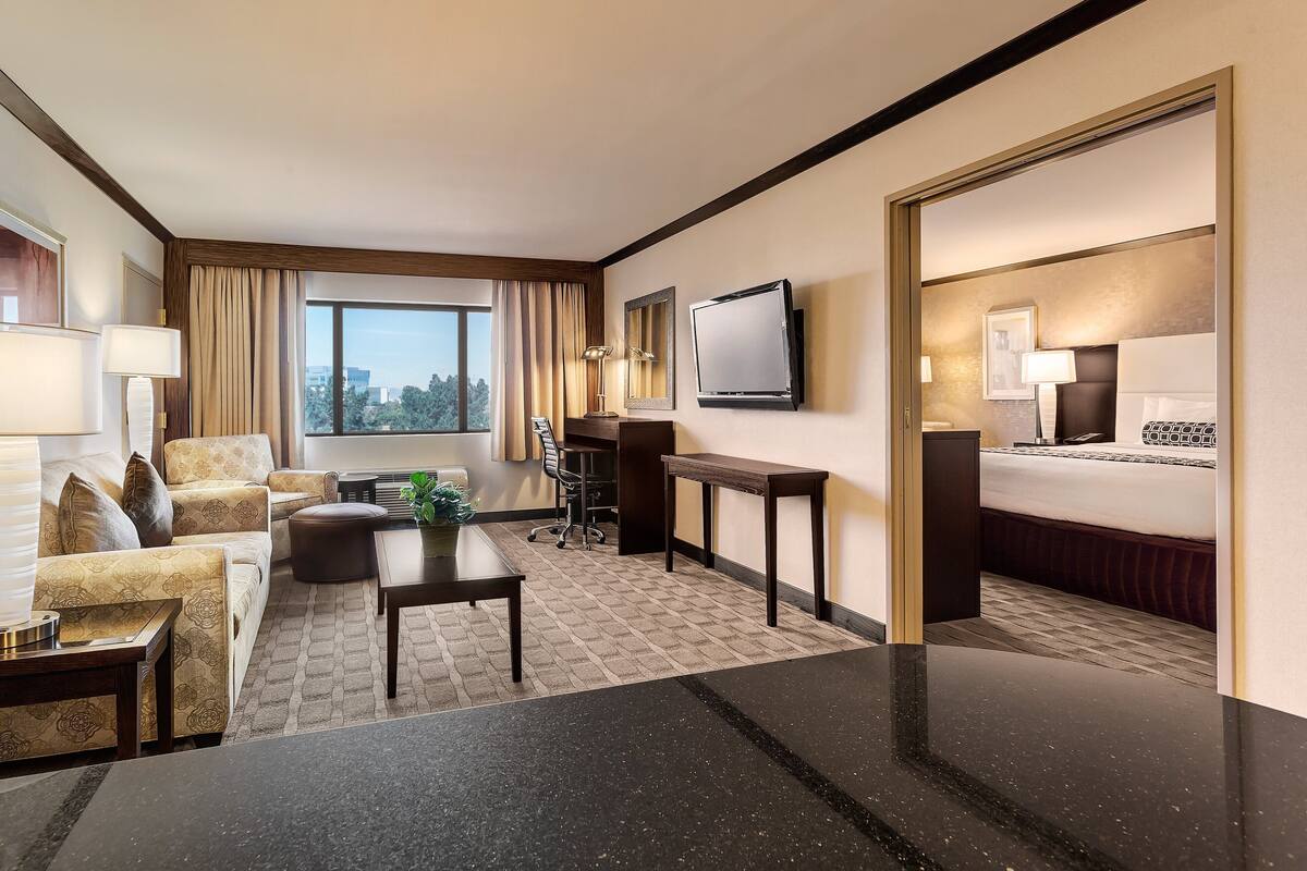 A hotel room with a sofa, armchair, dining table, and a bed.