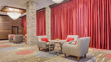 Un vestíbulo de hotel con cortinas rojas, pilares de piedra y mobiliario de mimbre.