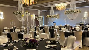 Un salón de banquetes con mesas redondas, sillas blancas y candelabros.