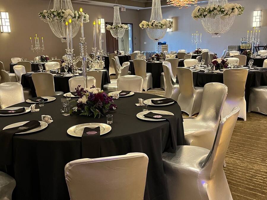 A banquet hall with round tables, white chairs, and chandeliers.