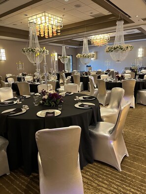 Un salón de banquetes con mesas redondas, sillas blancas y candelabros.