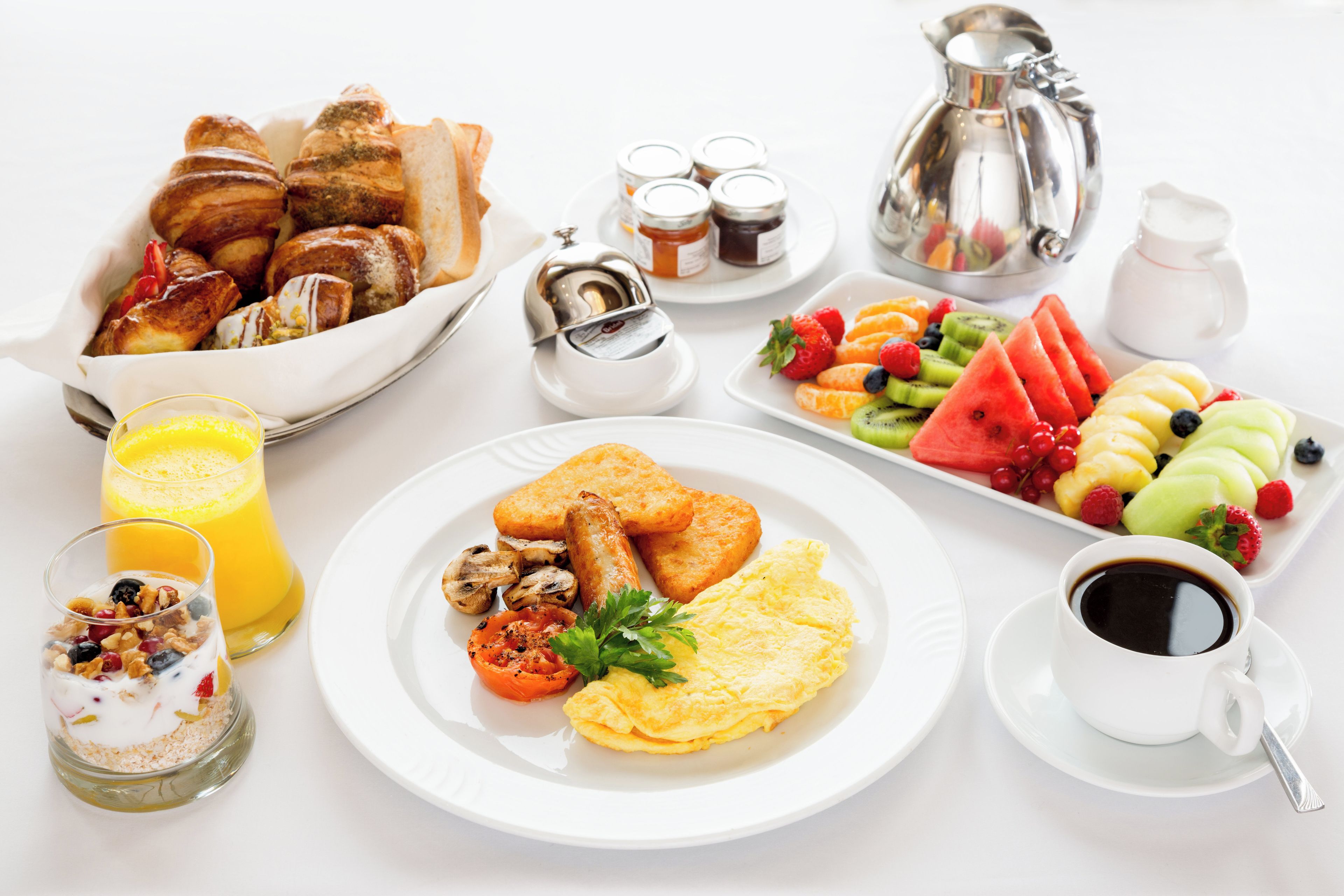 A breakfast table with various food items, a pitcher, and a cup of coffee.