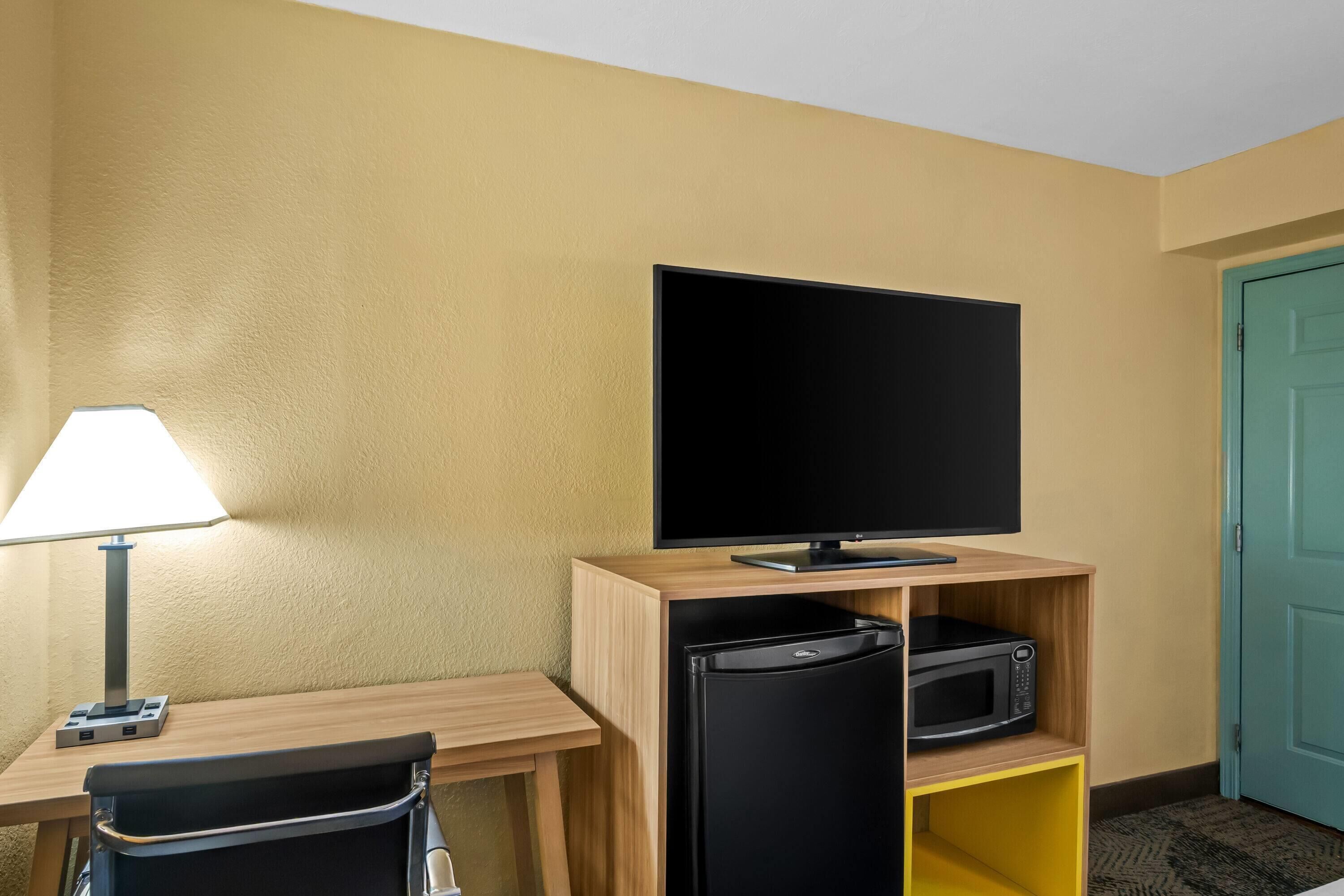 Una habitación de hotel con escritorio, televisión, lámpara y microondas.