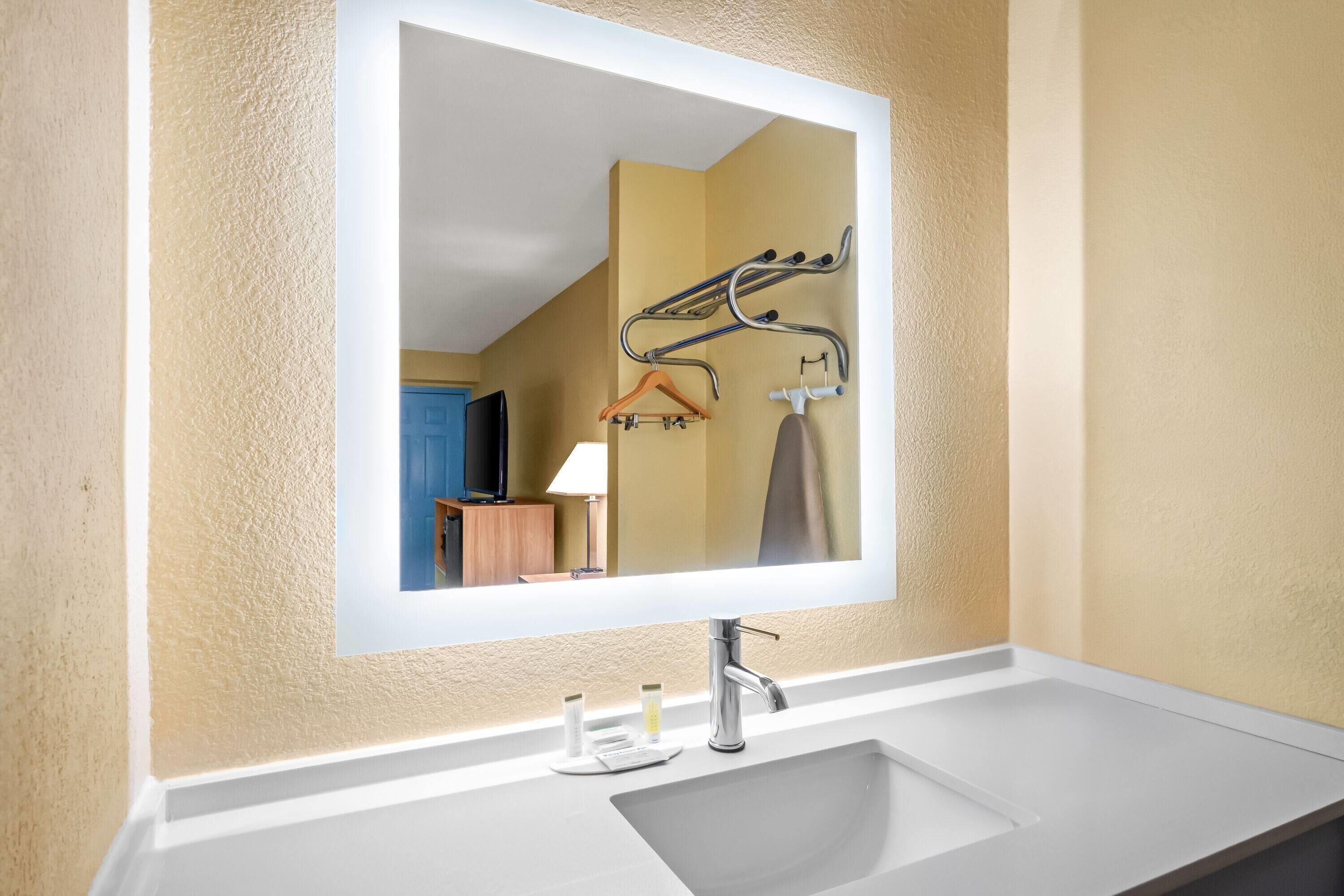 Une salle de bain avec un grand miroir, un lavabo blanc et un porte-serviettes.