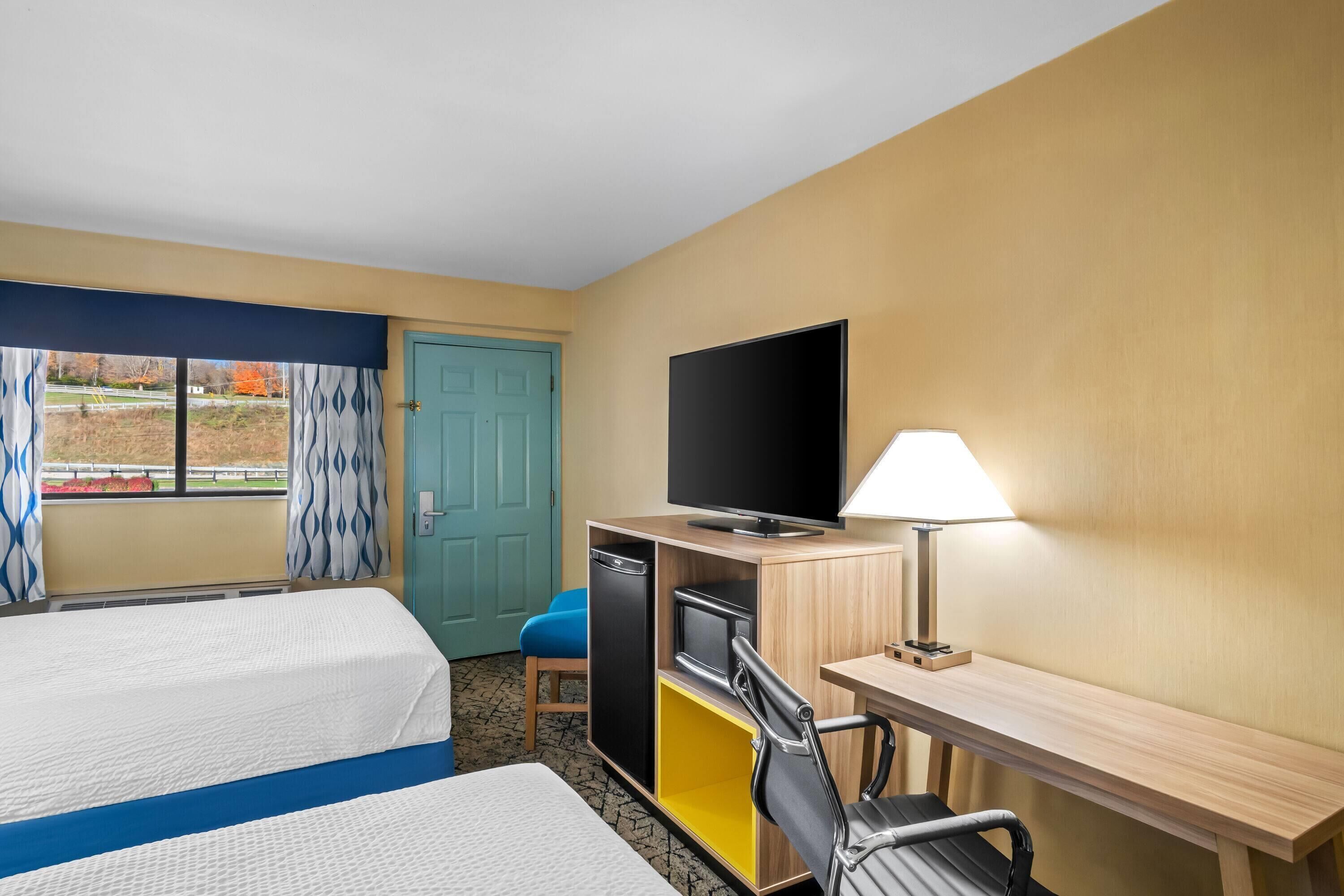 Ein Hotelzimmer mit zwei Betten, einem Schreibtisch, einem Sessel, einem Fernseher und einer Lampe.
