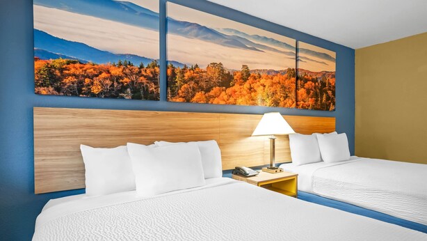 A hotel room with two beds, a wooden headboard, a nightstand with a lamp, and a large autumn forest mural on the wall. - Days Inn by Wyndham Renfro Valley Mount Vernon (Mount Vernon)