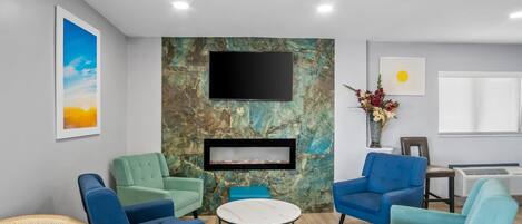 A modern lounge area with teal and blue upholstered chairs, a marble accent wall, a flat-screen TV, and a fireplace.