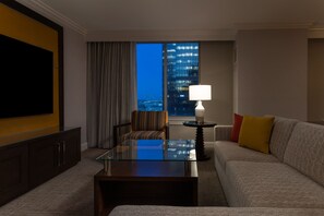 A hotel room with a large window, a sofa, a glass coffee table, a TV, and a lamp.