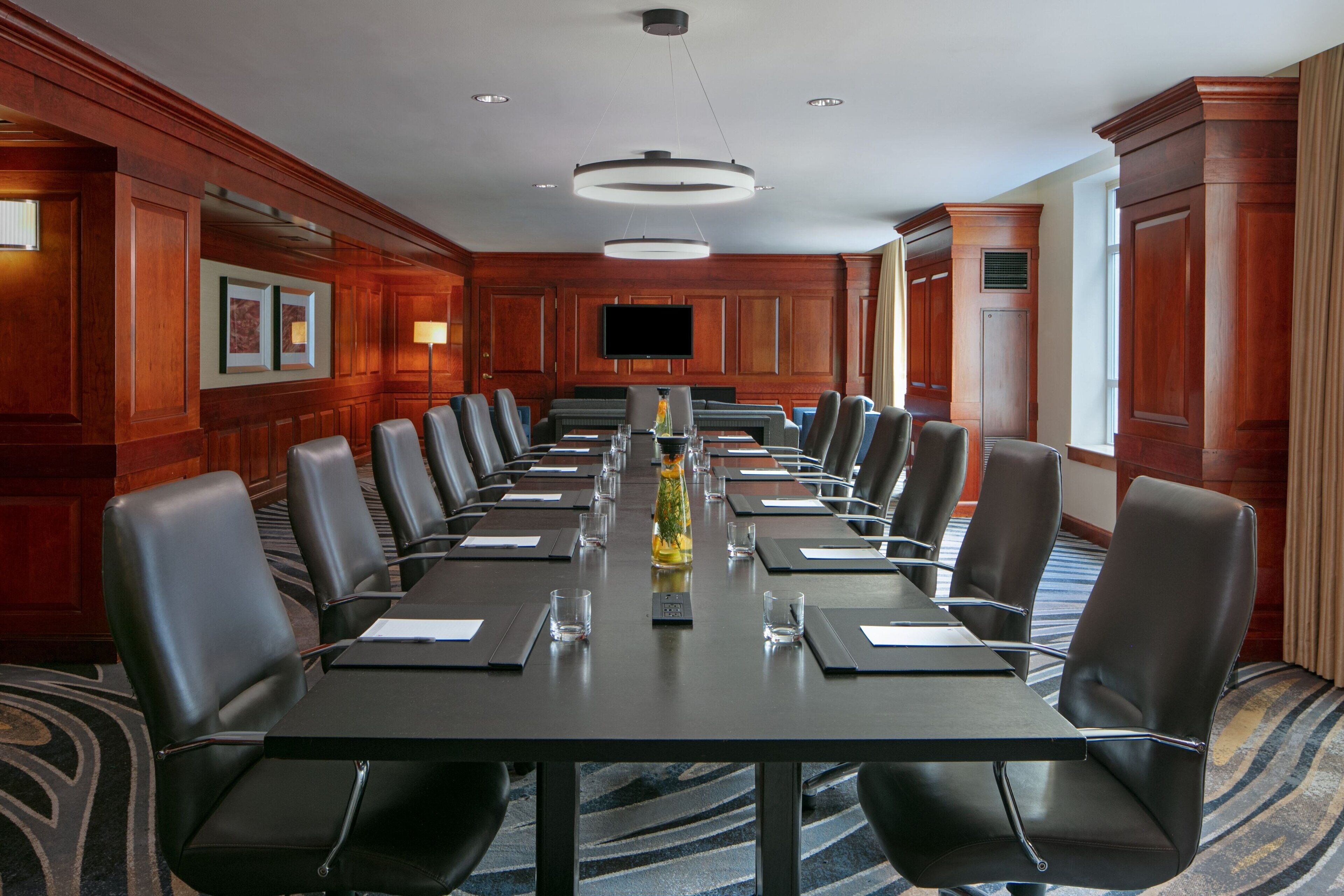 Un salón de conferencias con una mesa larga, varias sillas y una pantalla de televisión.