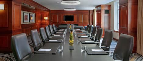 A conference room with a long table, multiple chairs, and a television screen.