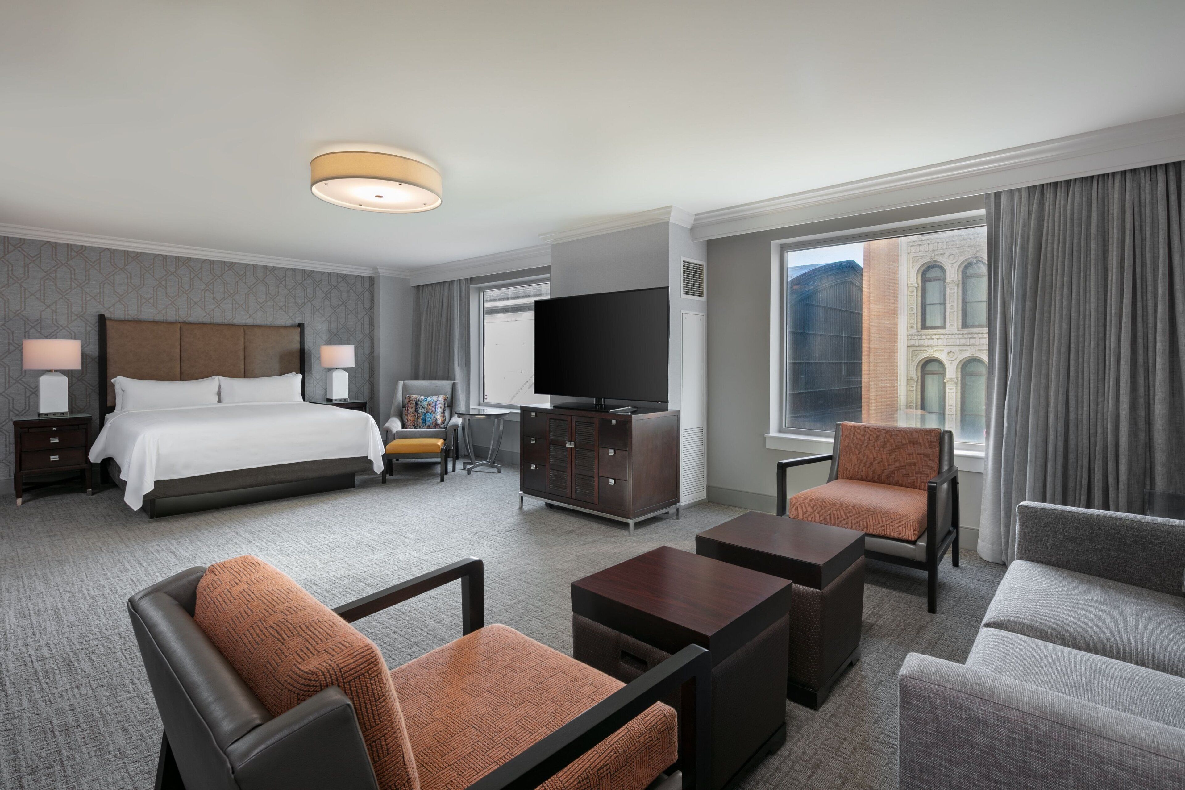 Une chambre d’hôtel moderne dotée d’un grand lit, d’une télévision à écran plat, d’un bureau et d’un coin salon avec deux fauteuils et un canapé.