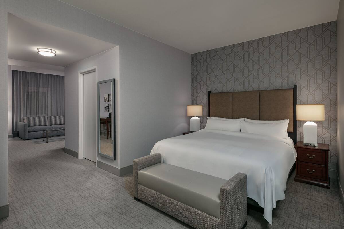 Une chambre d’hôtel avec un grand lit, deux tables de chevet avec des lampes, un canapé, un miroir et un mur décoré d’un motif.