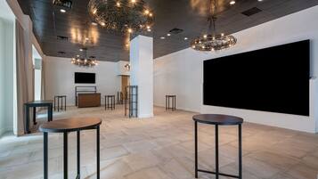 A spacious room with a large black screen, two round tables, and modern pendant lights.