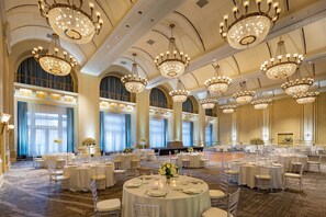 A large banquet hall with multiple round tables set for events, featuring chandeliers and elegant decor.