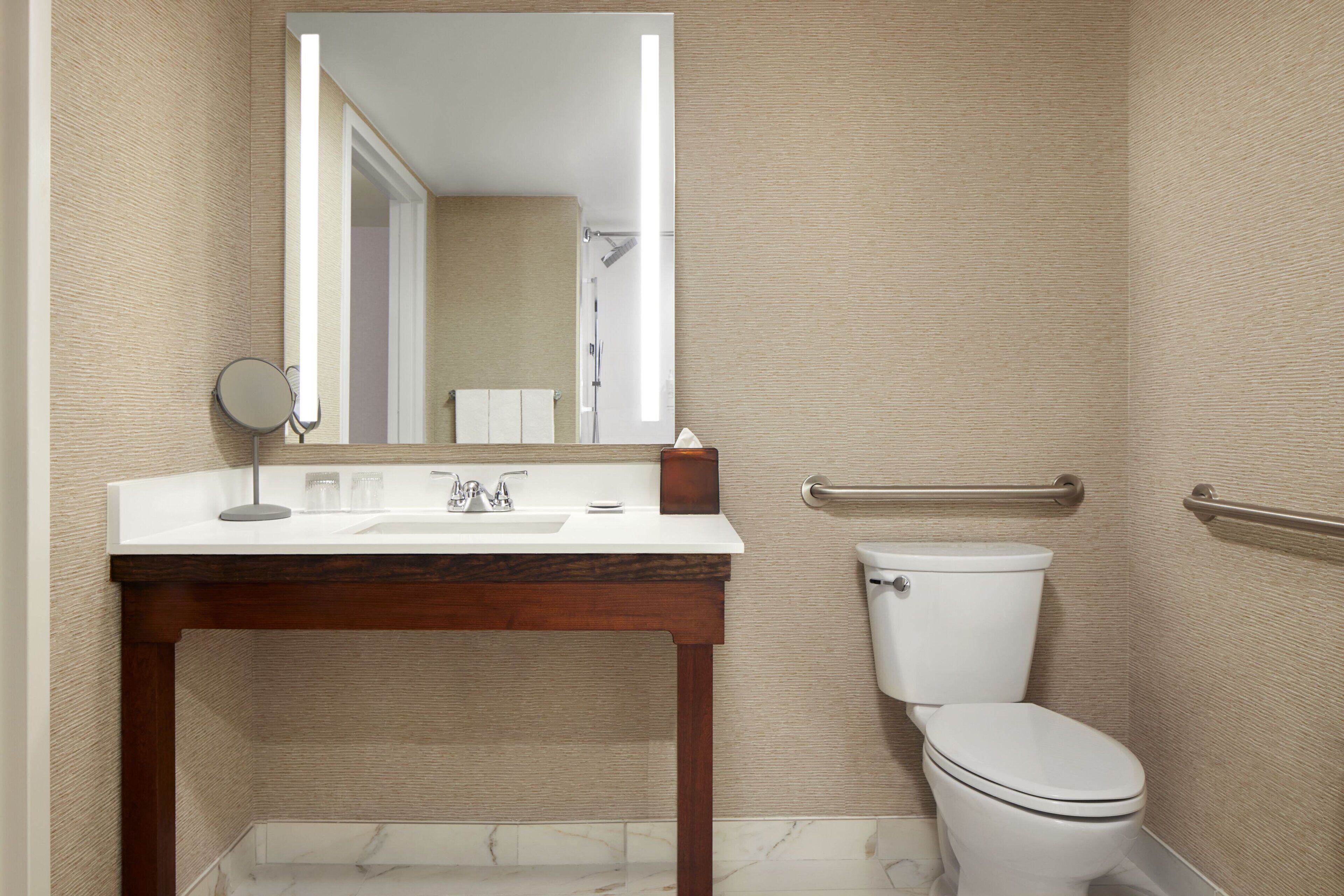Un baño con tocador de madera, un lavabo blanco, un espejo, un inodoro y un perchero para toallas.