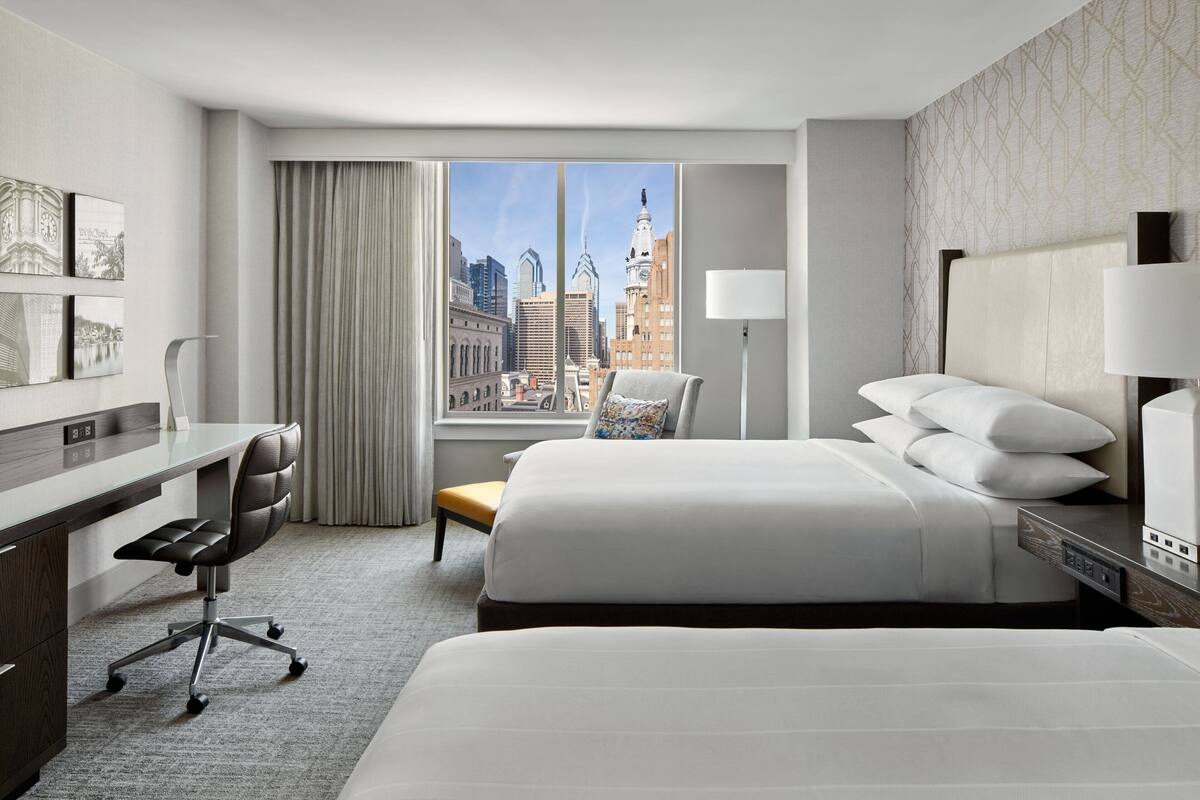 Une chambre d’hôtel avec un grand lit, un bureau et une chaise. Il y a une fenêtre donnant sur la ville.