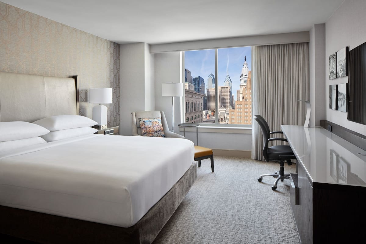 Une chambre d’hôtel moderne avec un grand lit, un bureau, une chaise et une vue sur le paysage urbain.