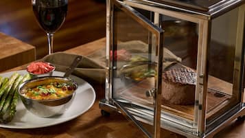 Uma mesa de jantar com uma vitrine de vidro contendo um bife, uma tigela de sopa e aspargos.