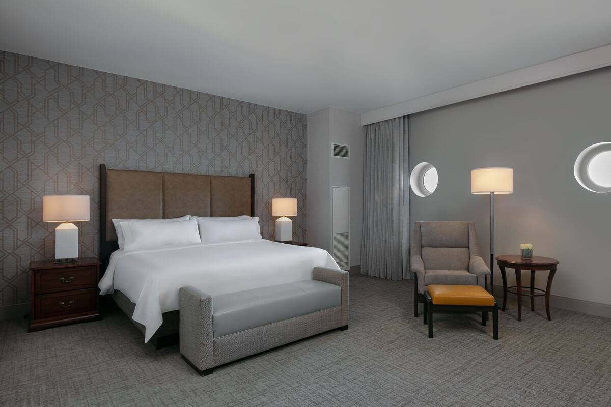 Une chambre d’hôtel comprenant un lit, des tables de chevet, une chaise, une petite table et une lampe.