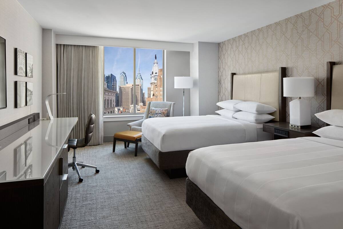 Une chambre d’hôtel avec deux lits, un bureau, une chaise et une vue sur le paysage urbain.