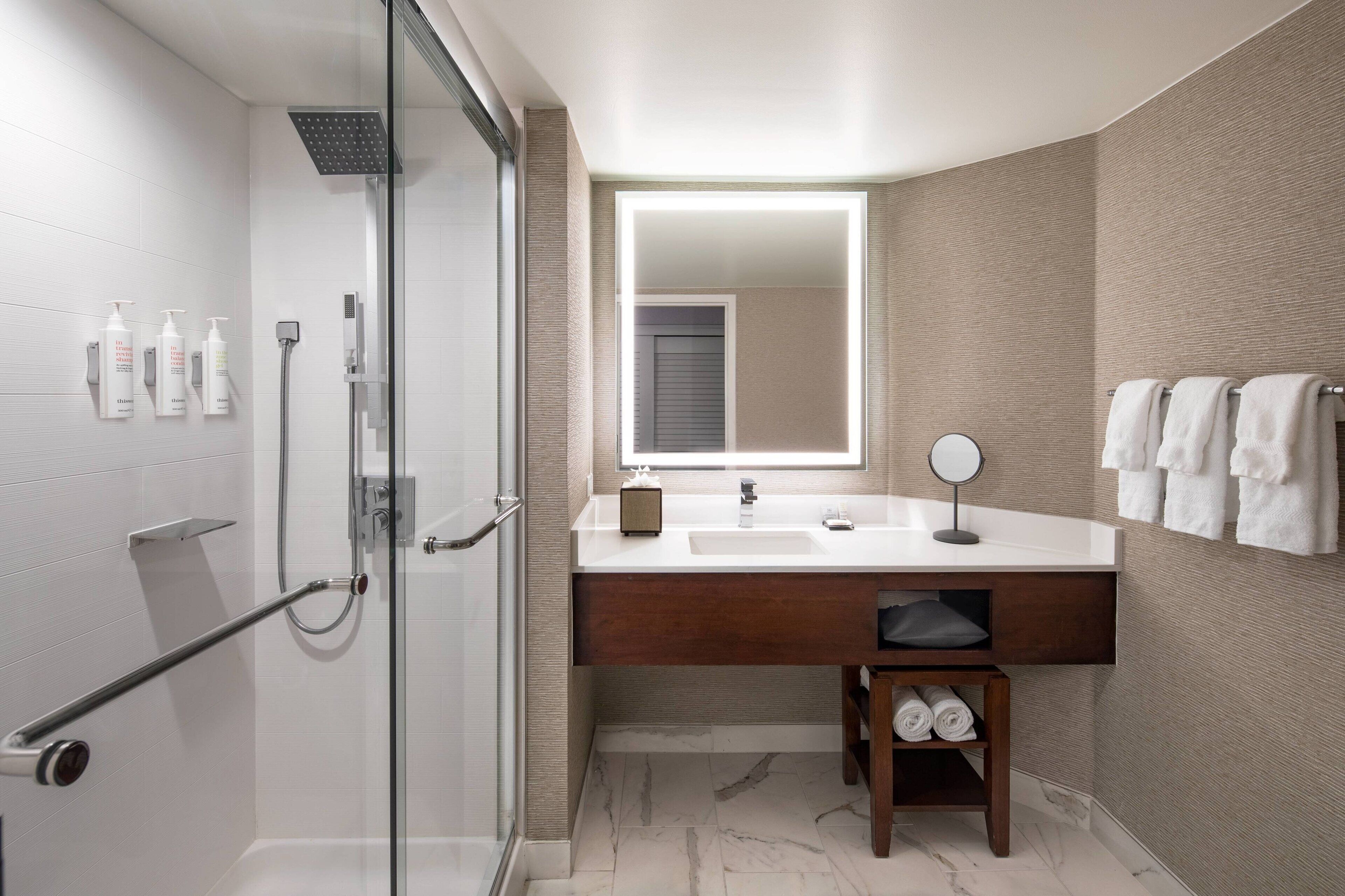 A modern bathroom with a glass shower enclosure, a white sink with a mirror, and a towel rack.