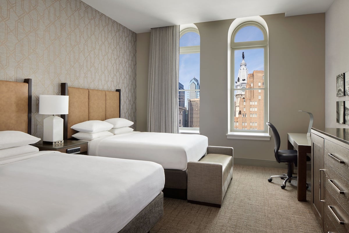 Une chambre d’hôtel avec deux lits, un bureau, une chaise et une vue sur le paysage urbain.