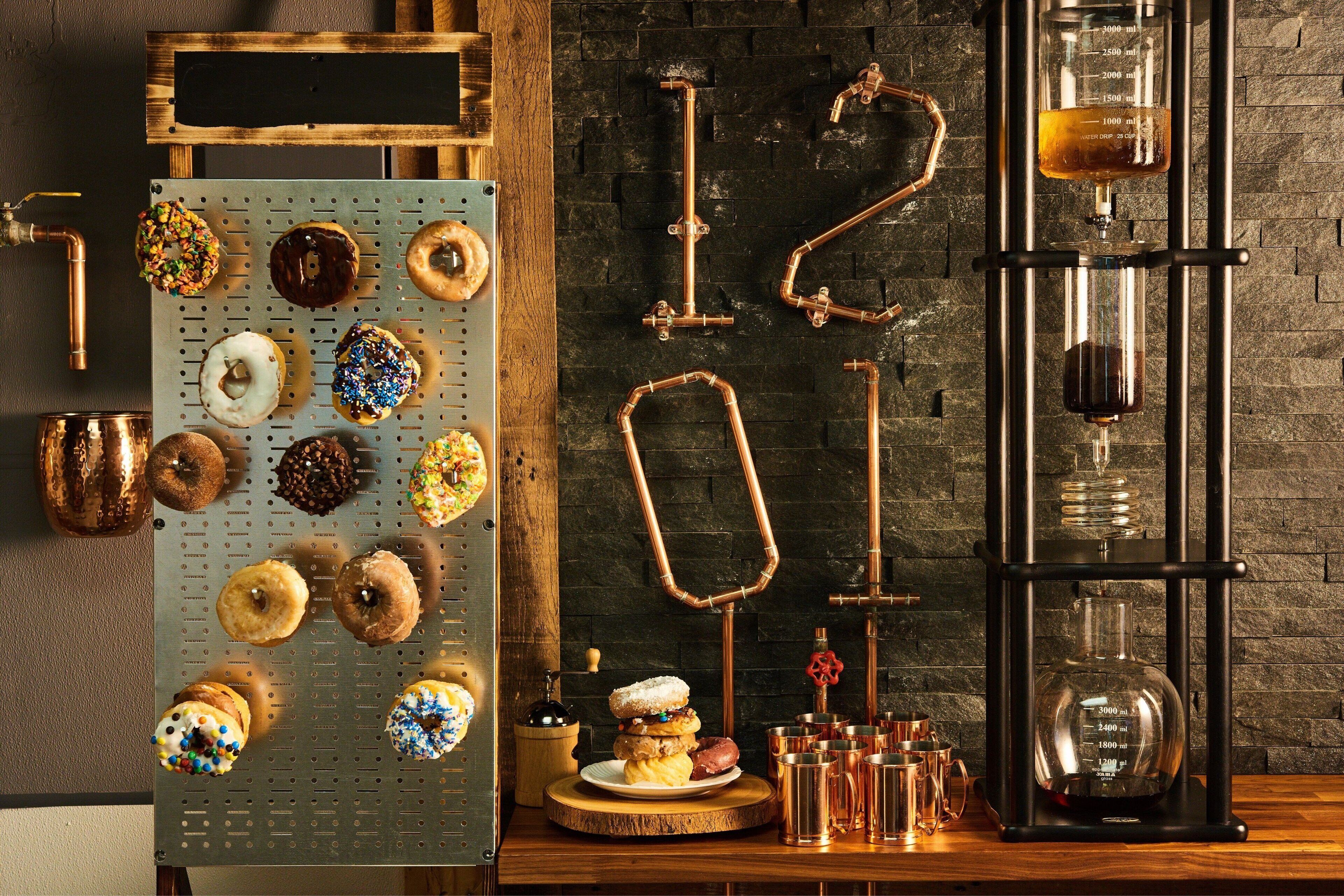 Une cuisine équipée d’une étagère en métal où sont disposés divers beignets, des tuyaux en cuivre et un appareil de distillation.