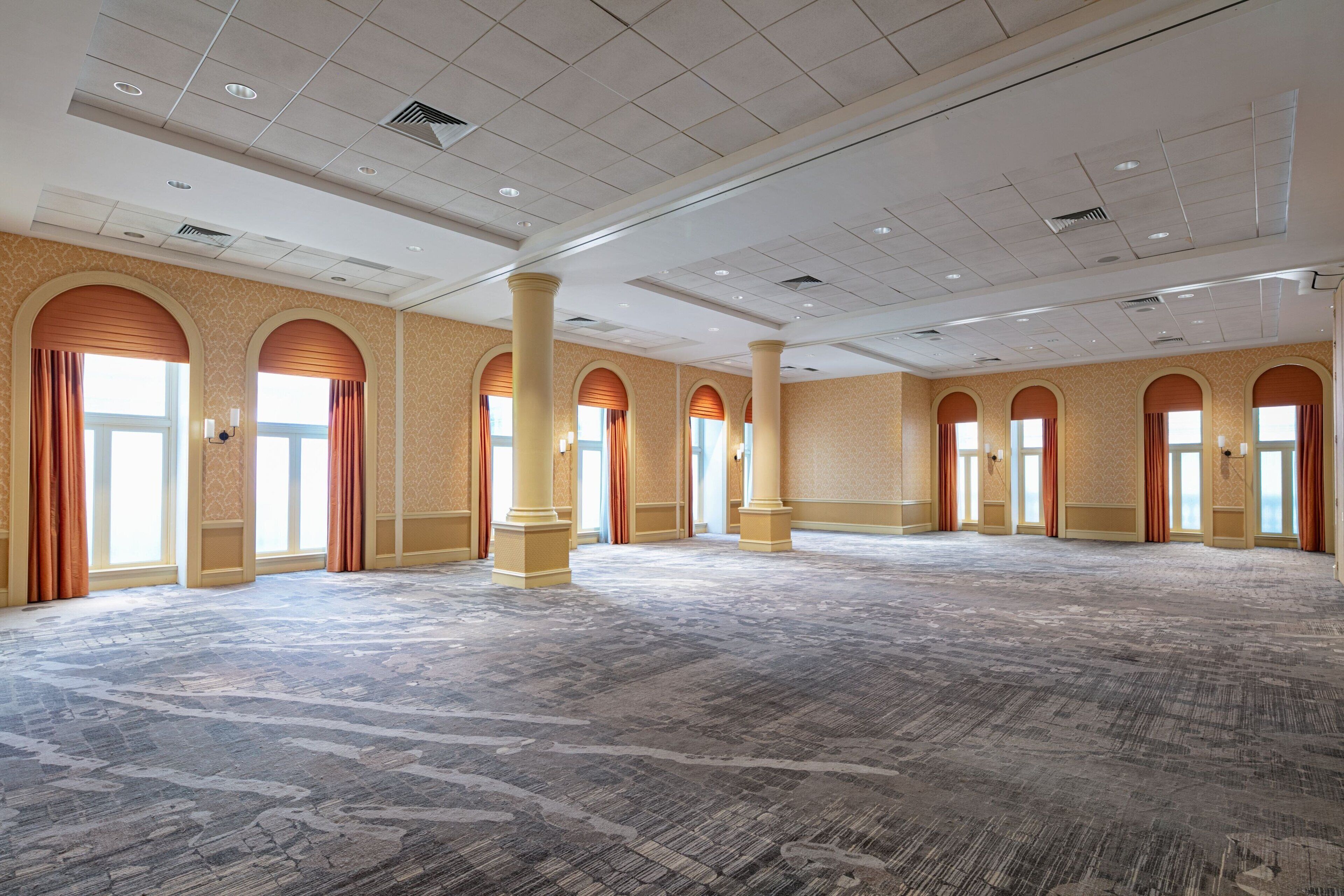 A spacious hall with high ceilings, large windows with curtains, and a patterned carpet.