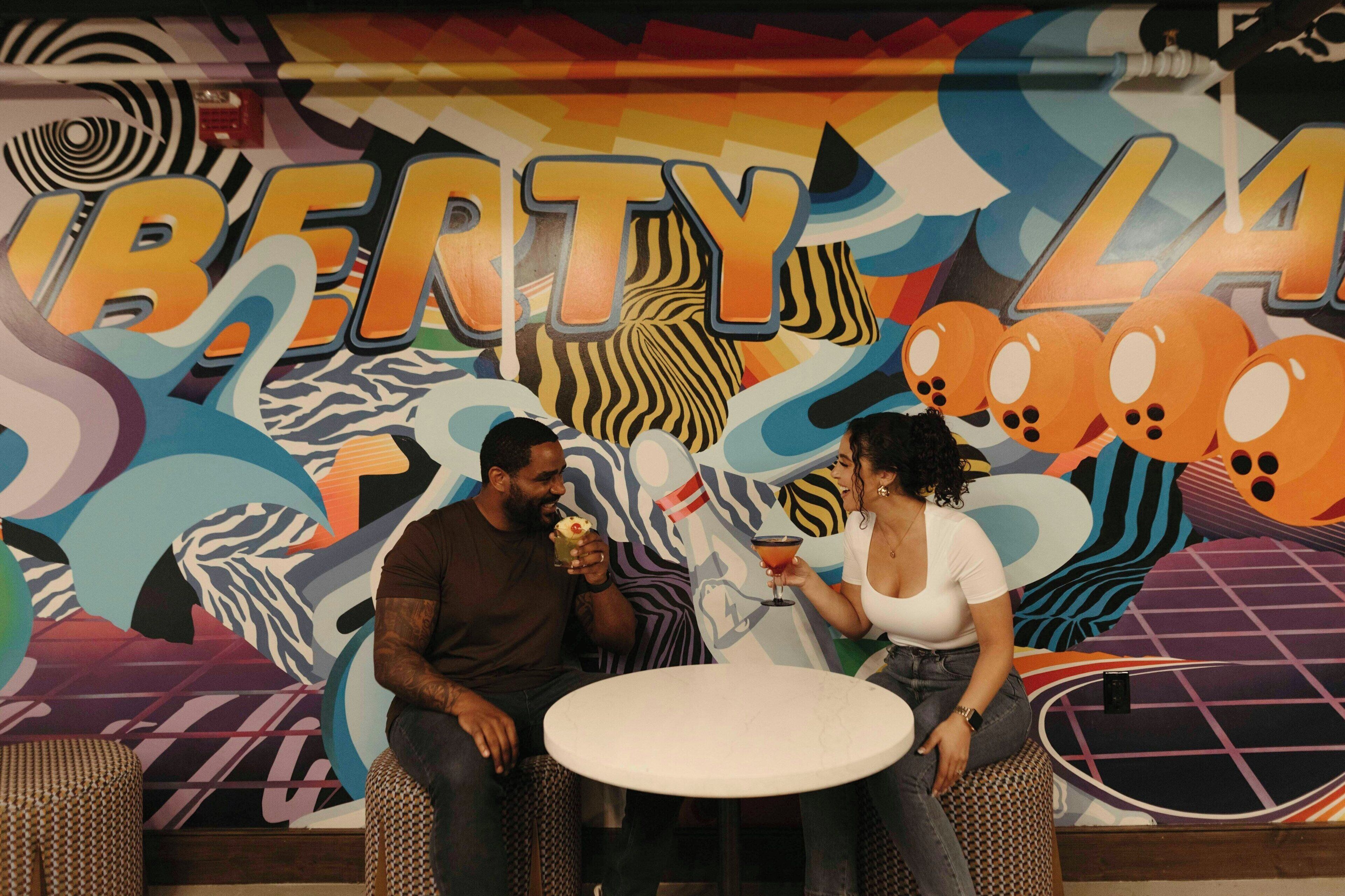 Two people sitting at a table in a room with a colorful mural featuring the word "LIBERTY" and abstract designs.