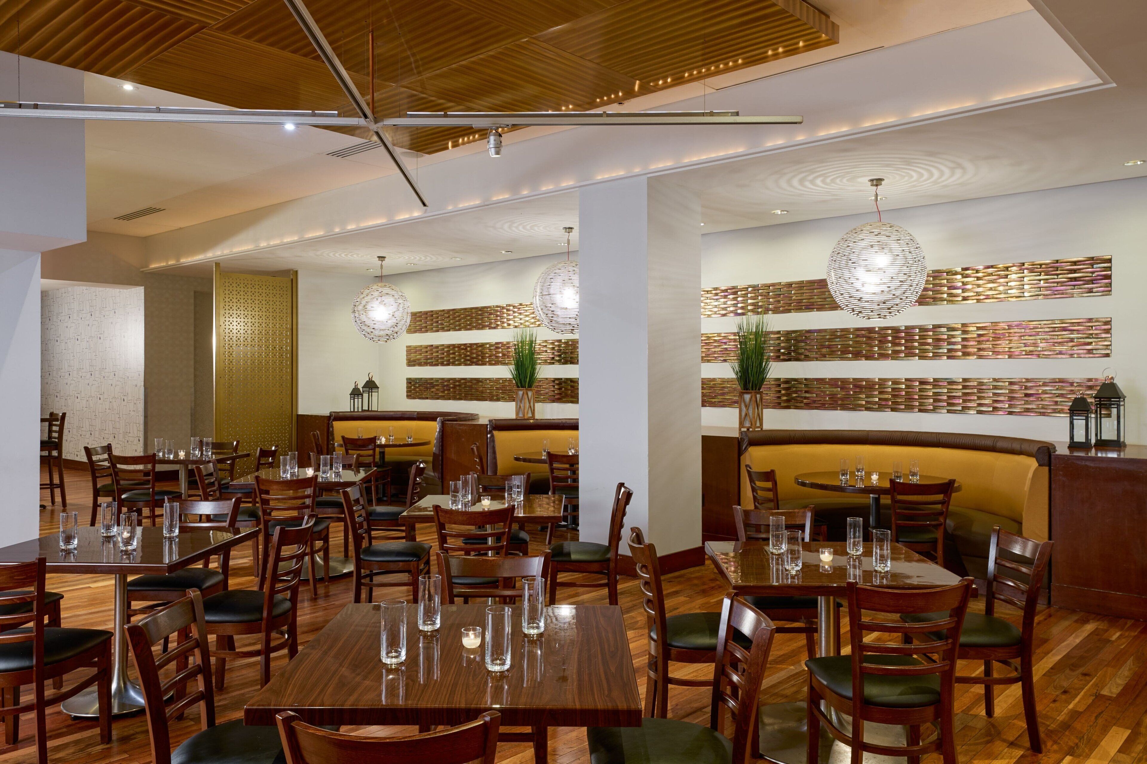 A restaurant with wooden tables and chairs, a high ceiling with recessed lighting, and decorative wall panels.