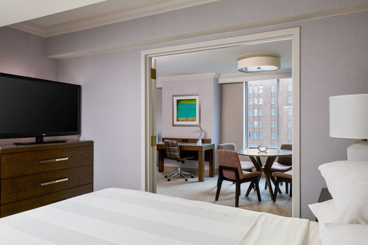 Une chambre d’hôtel comprenant un lit, un téléviseur posé sur une commode, un bureau avec une chaise et un coin repas avec une table et des chaises.