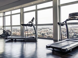 A gym with treadmills and a stationary bike, large windows, and a city view. - Mercure Hotel Luedenscheid (Luedenscheid)
