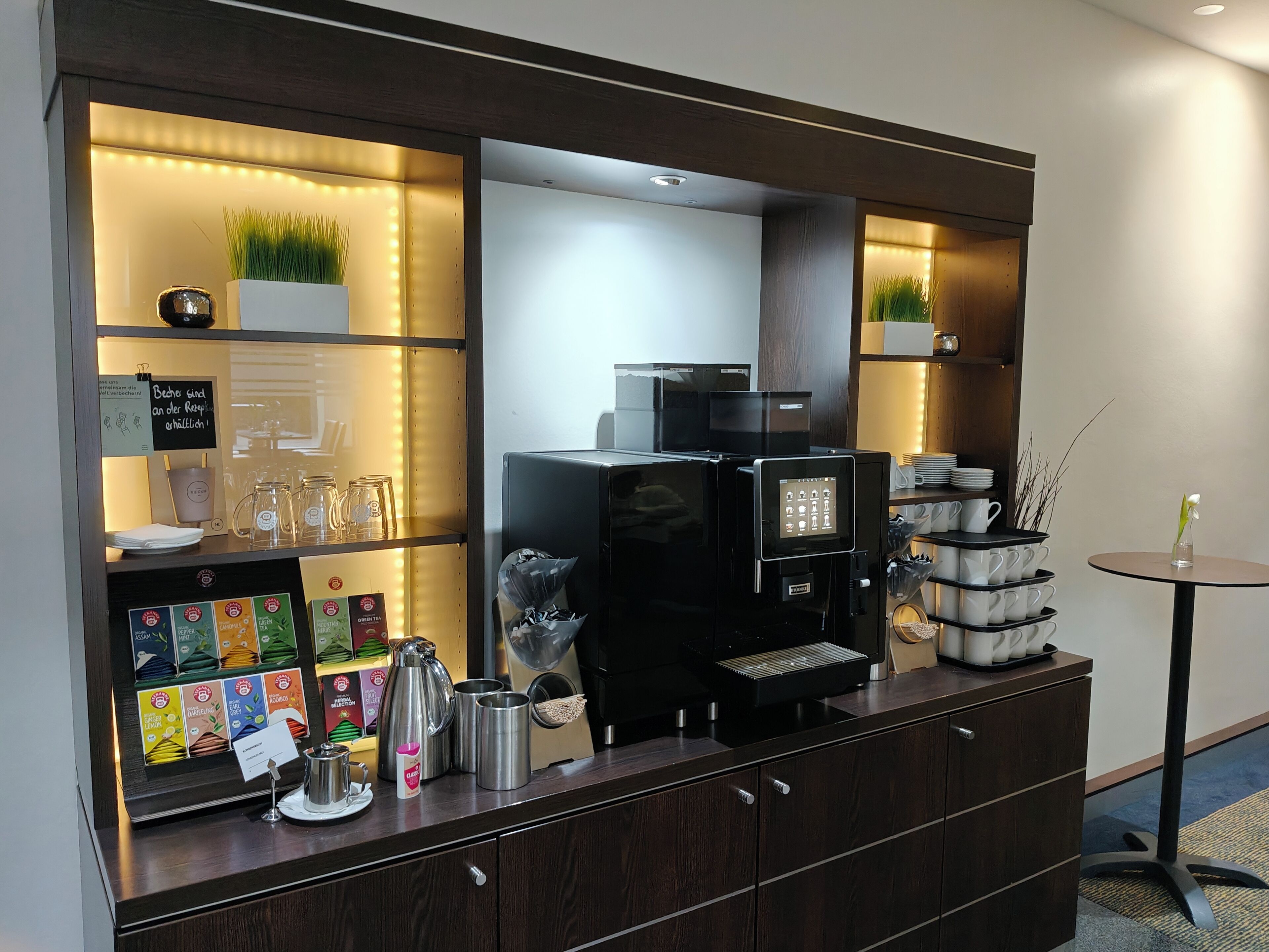 Un angolo caffè con macchina da caffè, distributori di tè e una selezione di bustine di tè.