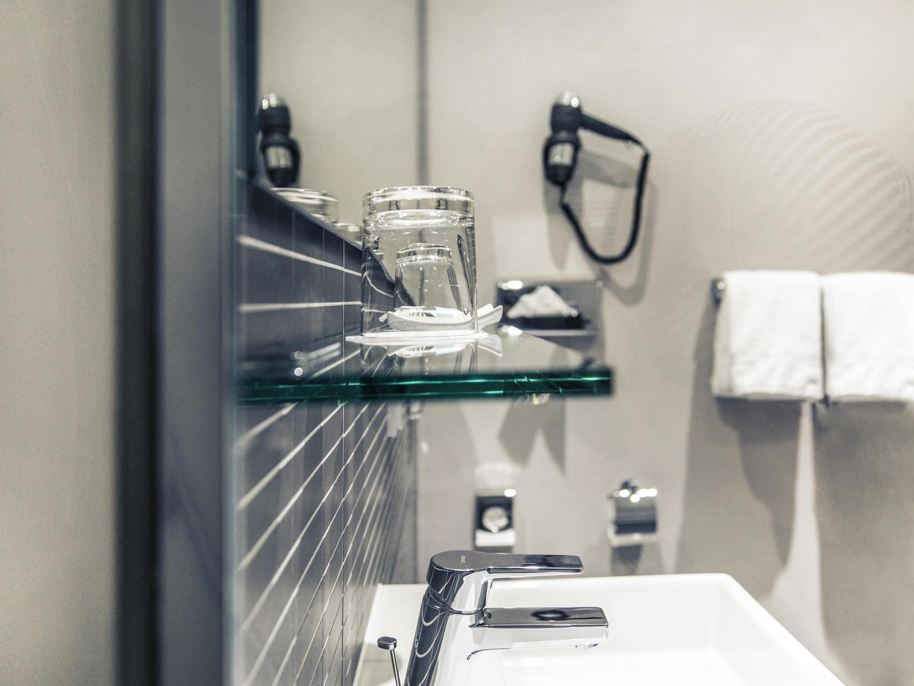 Un baño con repisa de vidrio que sostiene un vaso, un perchero con una toalla y un espejo.