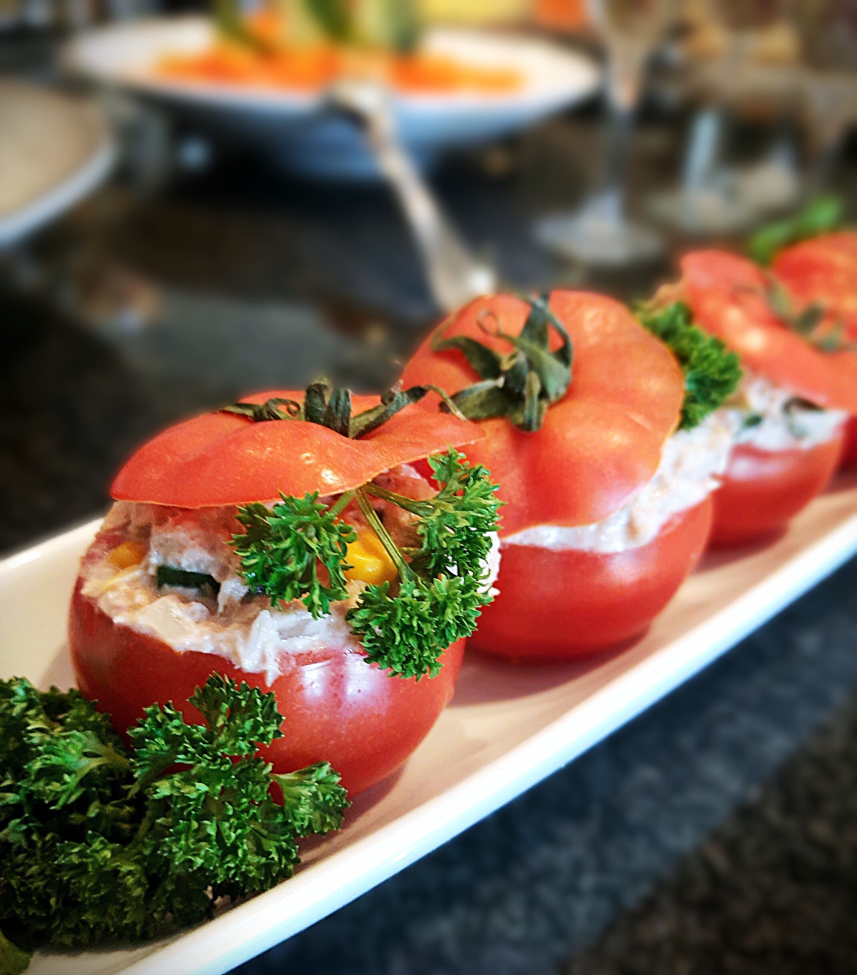 A row of stuffed tomatoes on a white plate, garnished with parsley.
