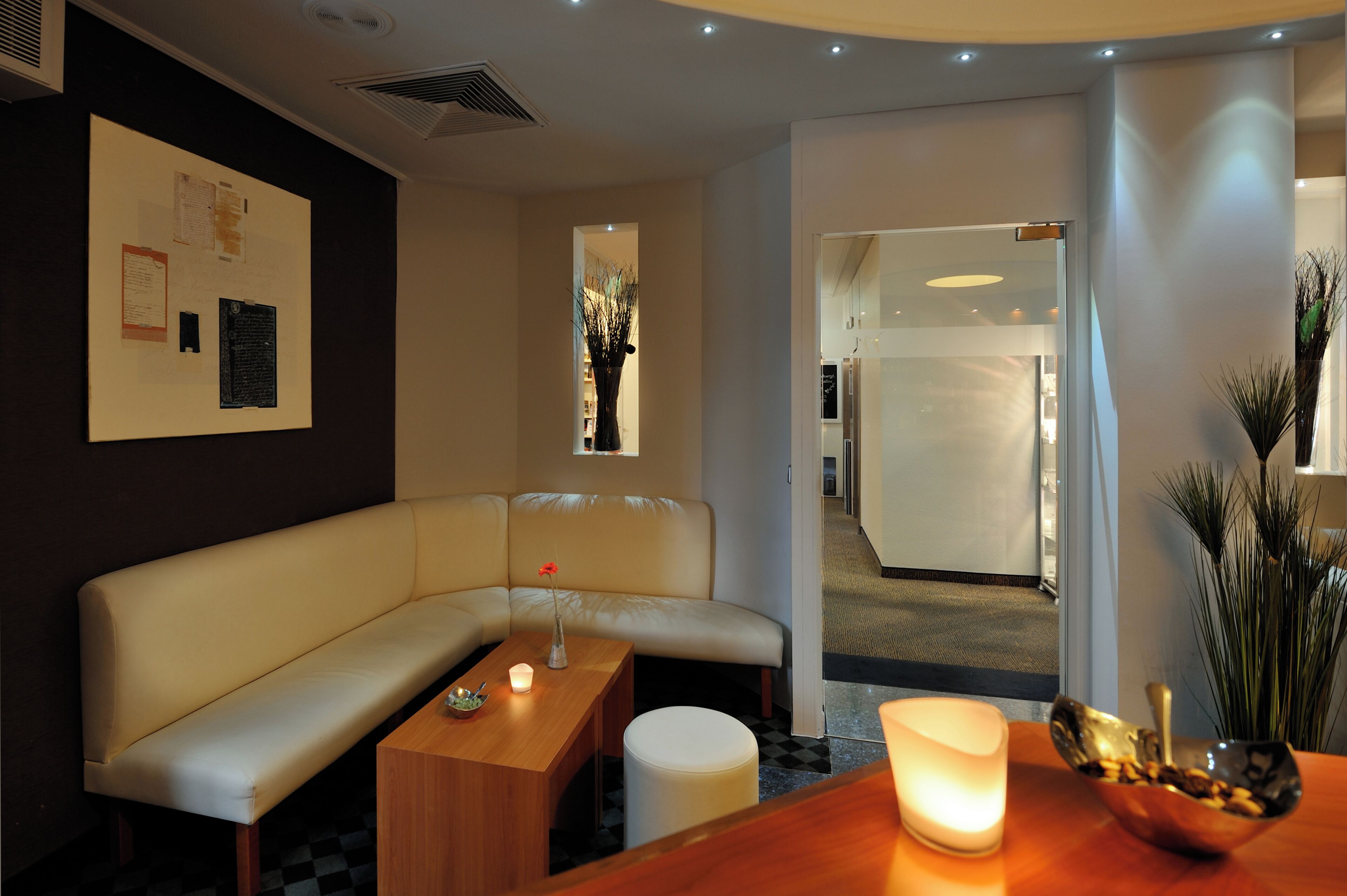 Ein modernes Hotelzimmer mit einer weißen Couch, einem Holztischchen mit einer Kerze, einem kleinen Tisch mit einer Schale und einer Vase mit einer Blume.