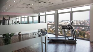 A spacious gym with a treadmill and exercise equipment, large windows offering a city view, and a wooden floor. - Mercure Hotel Luedenscheid (Luedenscheid)