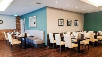 A modern dining area with wooden flooring, white and beige seating, and teal and beige walls.