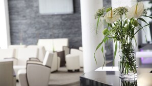 A modern lobby with a clear vase of flowers on a black table, white sofas, and a grey textured wall. - Mercure Hotel Luedenscheid (Luedenscheid)