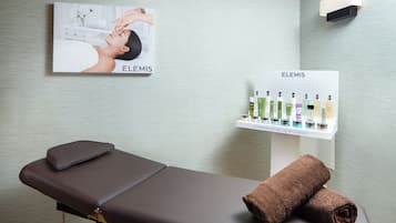 A spa treatment room with a massage table, a towel, and a shelf displaying Elemis skincare products.