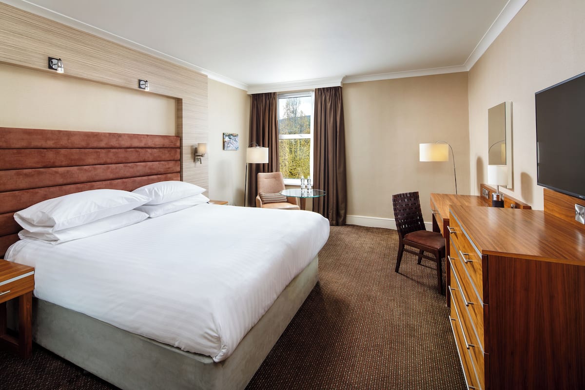 A hotel room with a large bed, a wooden dresser, a desk, and a chair.