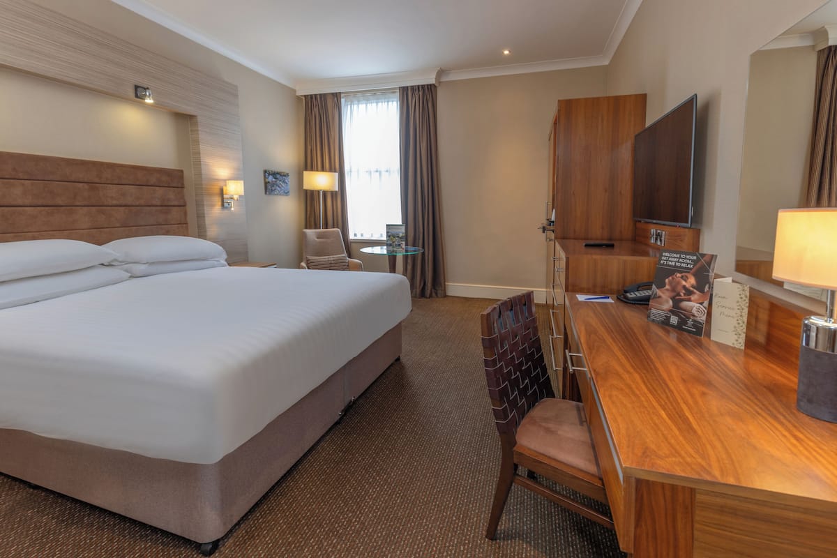 A hotel room with a large bed, a desk with a chair, a TV, and a small table.