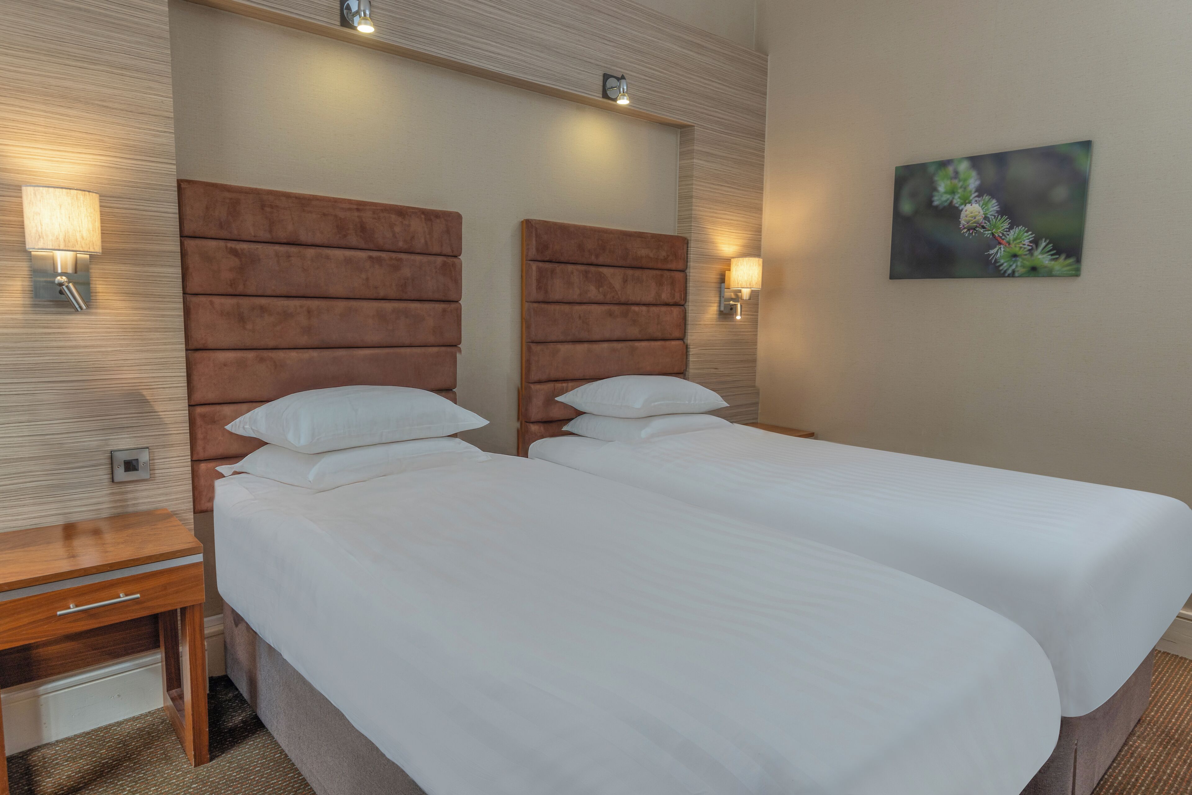 A hotel room with two beds, a nightstand, and wall-mounted lamps.
